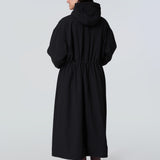 Back view of a woman wearing a black hooded long raincoat with yellow zipper.