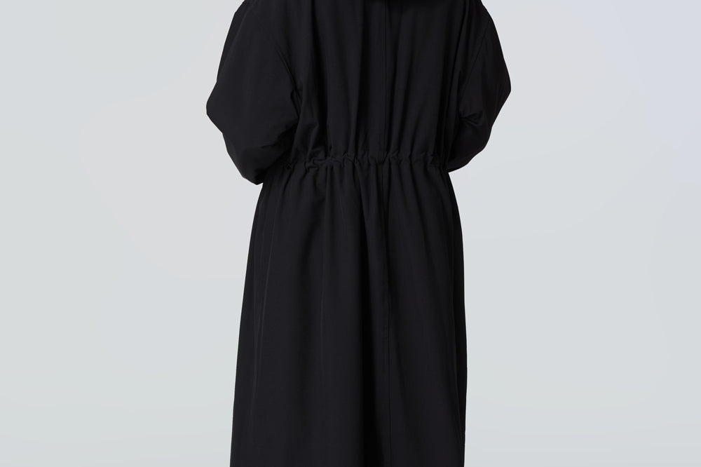 Back view of a woman wearing a black hooded long raincoat with yellow zipper.