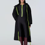 Front view of a woman wearing a black hooded long raincoat with yellow zipper and black catsuit with yellow zipper.