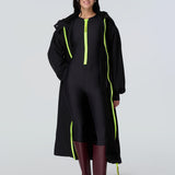 Front view of a woman wearing a black hooded long raincoat with yellow zipper and black catsuit with yellow zipper.