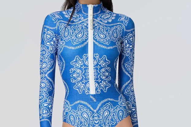 Woman wearing a long-sleeve bodysuit in a blue bandana print with white front zipper.