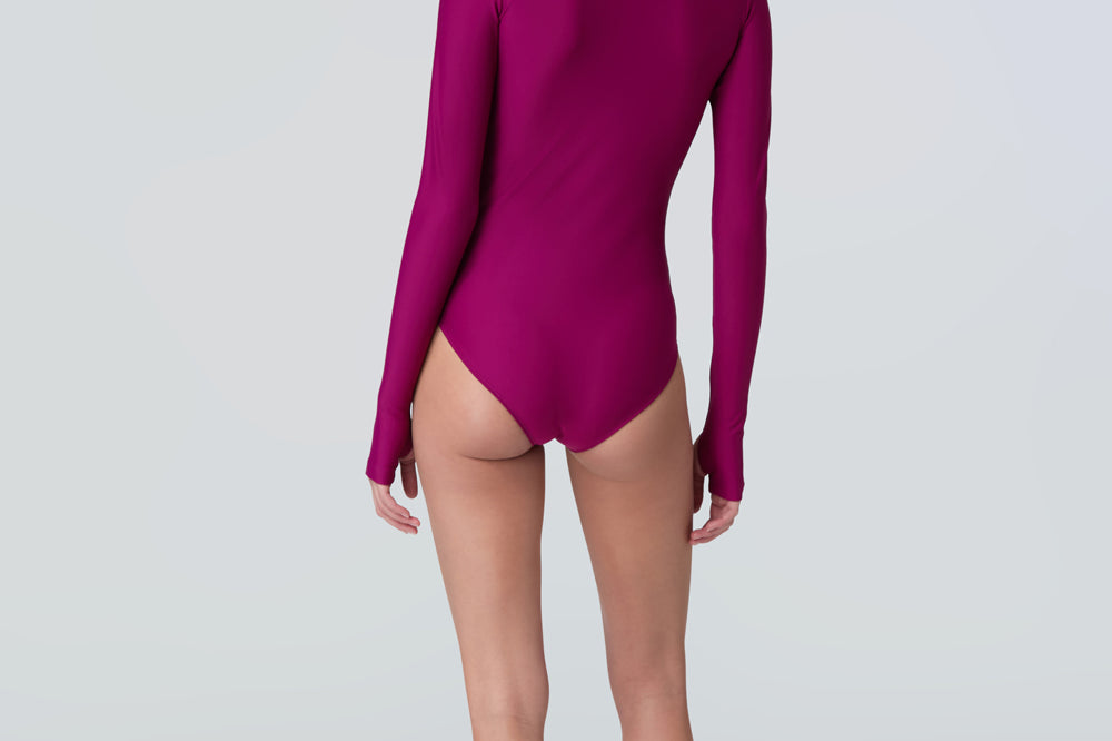 Back view of a woman wearing a long sleeve bodysuit in dark berry with a pink front zipper.