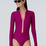 Front view of a woman wearing a long sleeve bodysuit in dark berry with a pink front zipper.