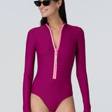 Front view of a woman wearing a long sleeve bodysuit in dark berry with a pink front zipper.