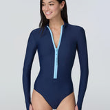 A woman wearing a long-sleeve navy blue one-piece swimsuit with a light blue front zipper.