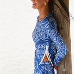 A woman in a blue and white  bandana-print long sleeve top with side zipper and pants.