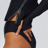Close up left side view of model wearing Watskin Sasha long sleeve rash guard tee and high cut Belle bikini brief in Black