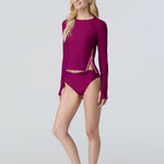 Woman wearing a long sleeve sun protective swim tee and bikini bottom in dark berry.