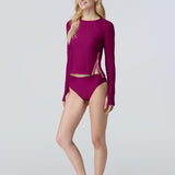 Woman wearing a long sleeve sun protective swim tee and bikini bottom in dark berry.