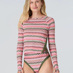 Full body front view of a woman wearing a pink and green wavy striped patterned long sleeve swim top with green statment side seam zipper and bikini bottom with green trim on a white background