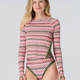 Full body front view of a woman wearing a pink and green wavy striped patterned long sleeve swim top with green statment side seam zipper and bikini bottom with green trim on a white background