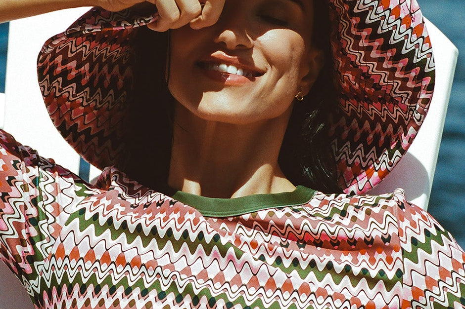 Pink & green wavy stripe sun hat, swim top with green cuffs, bikini bottom, dock by water