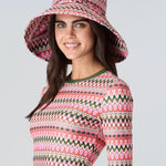 Woman wearing a pink and green wavy striped patterned wide brimmed sun hat, short sleeve swim top with green sleeve cuff