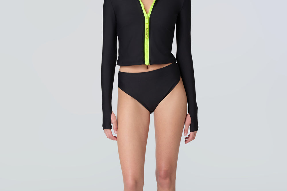 Front view of a woman wearing long sleeve mock neck zip front black rashguard with a yellow zipper and black bikini bottom.