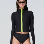 Front view of a woman wearing long sleeve mock neck zip front black rashguard with a yellow zipper and black bikini bottom.