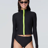Front view of a woman wearing long sleeve mock neck zip front black rashguard with a yellow zipper and black bikini bottom.