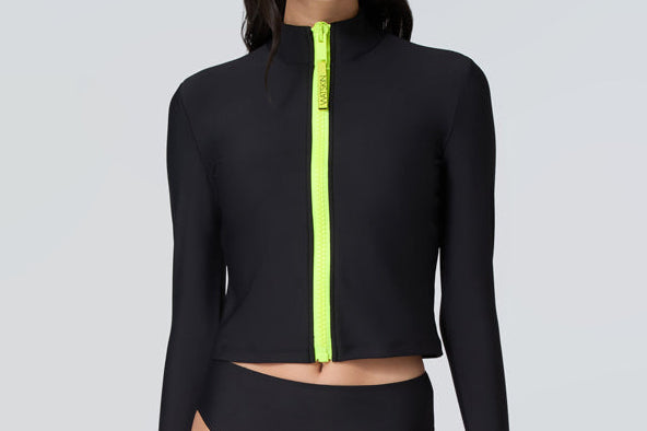Front view of a woman wearing long sleeve mock neck zip front black rashguard with a yellow zipper and black bikini bottom.