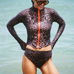 Woman wearing a long sleeve leopard print zip front rashguard and bikini bottom in the ocean.