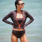 Woman wearing a long sleeve leopard print zip front rashguard, bralette, and bikini bottom in the ocean.
