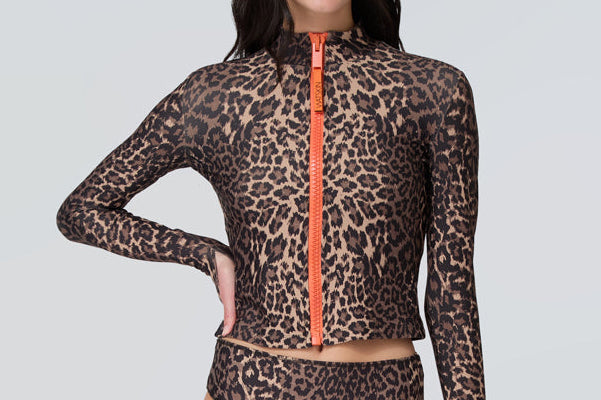 Front view of a woman wearing a long sleeve leopard print zip front rashguard and bikini bottom.